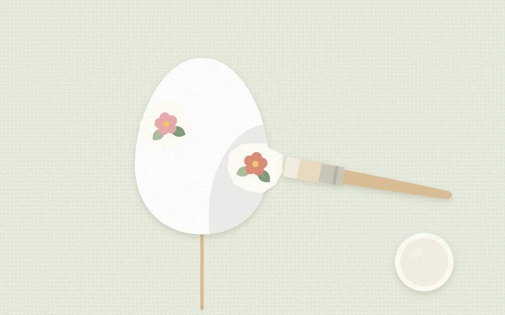 An egg on a skewer with a floral motif half applied and a flat soft brush smoothing it