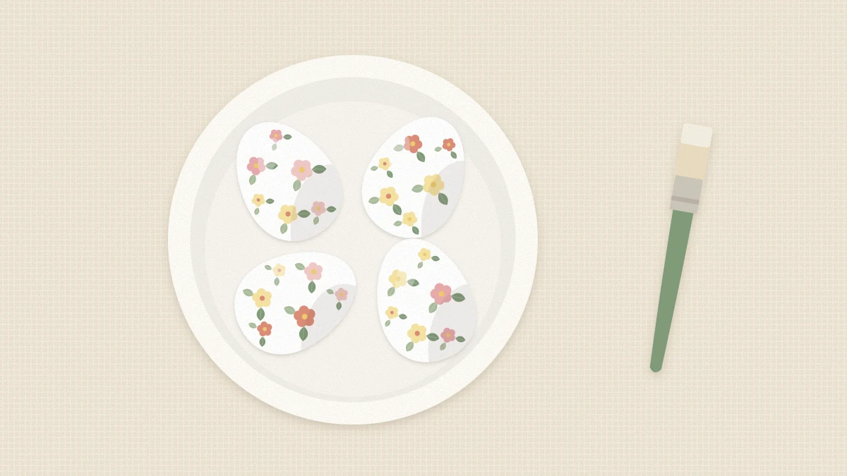 Four eggs covered in small floral paper motifs resting in a shallow ceramic dish with a soft brush beside it
