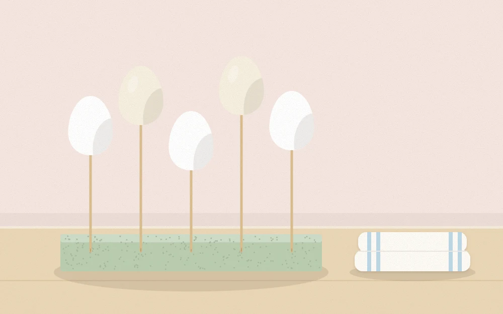Blown eggshells drying upright on wooden skewers in a foam block beside a towel