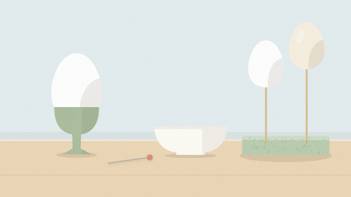 White egg upright in an egg cup with a pin and small bowl, and two emptied eggshells drying on skewers