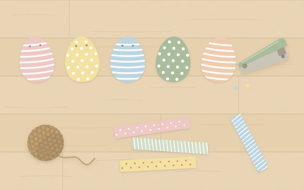 Cut paper eggs in a row on a table with hole punch, twine and strips of patterned paper