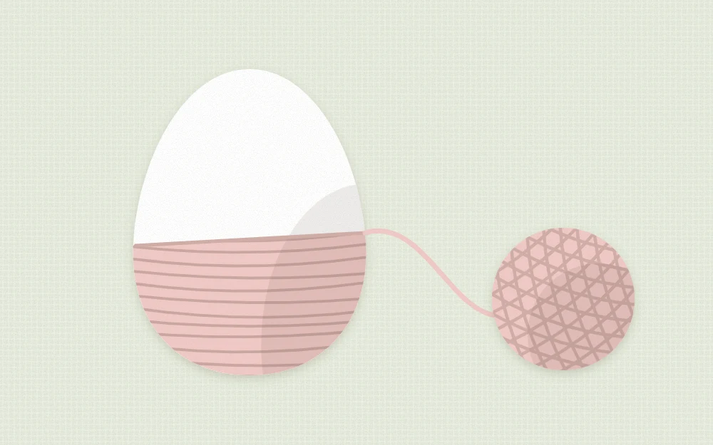 Egg half wrapped in yarn from the wide end, spiraling upward, with a ball of yarn beside it
